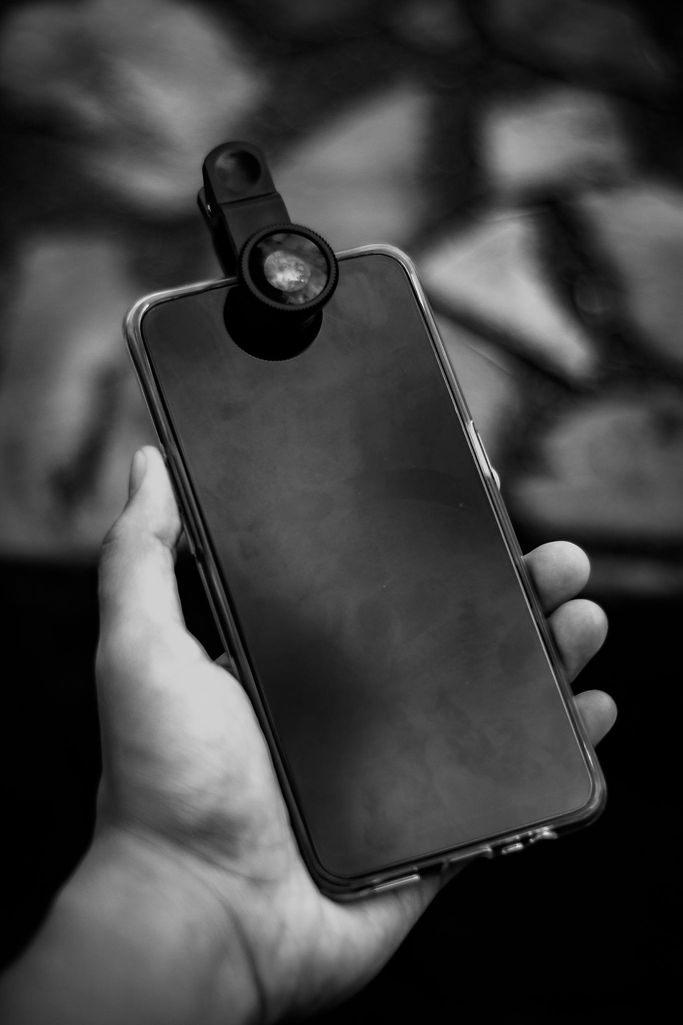 From above of black and white crop anonymous man showing mobile phone with attached optical lens